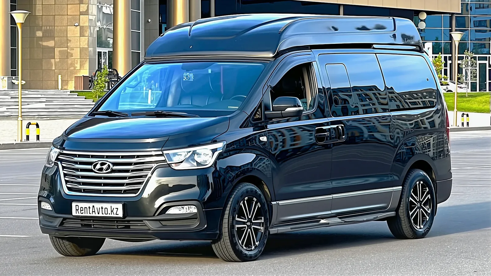 Тёмный минивэн Hyundai Grand Starex VIP стоит у стеклянного фасада офисного здания в Астане